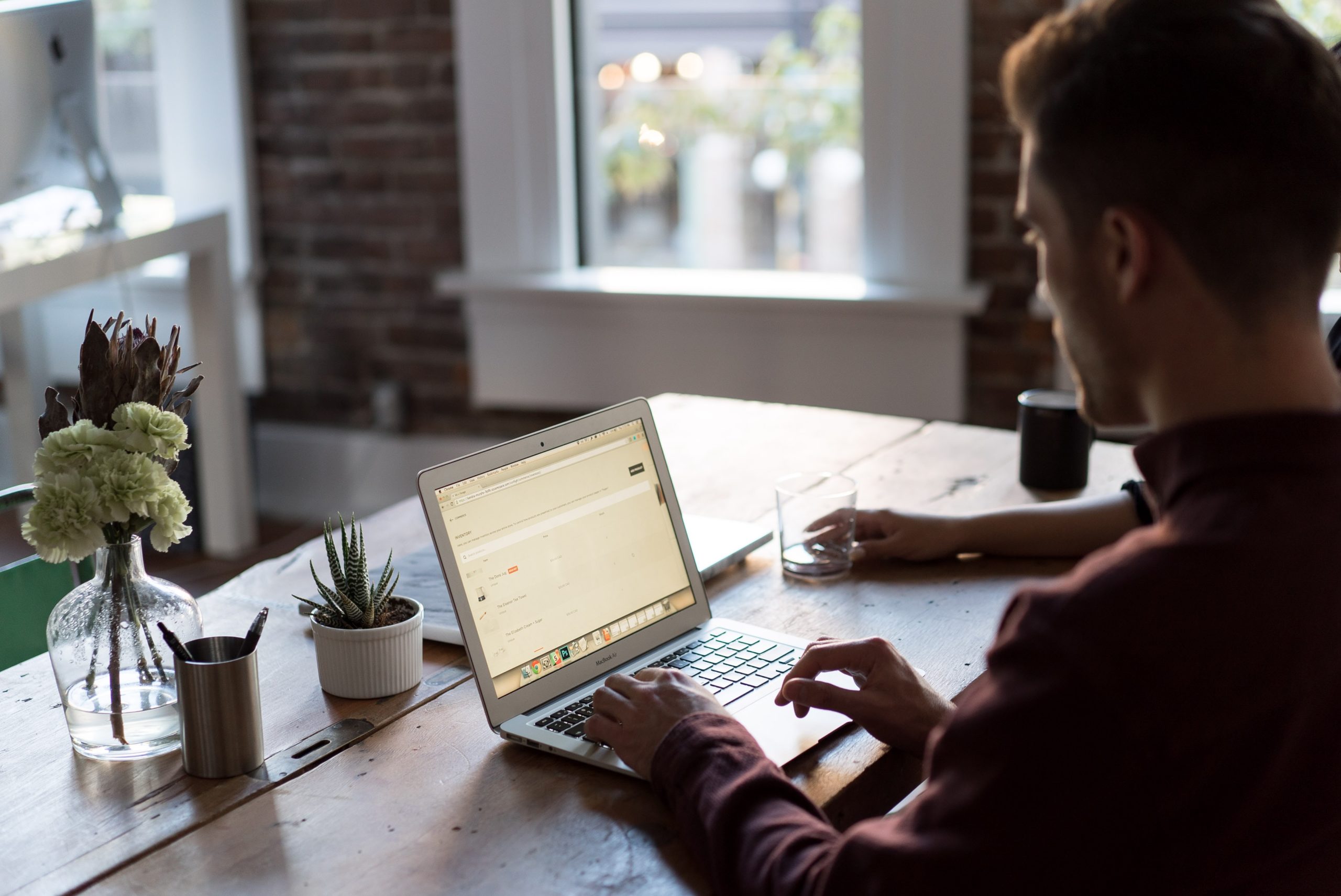 Over the Shoulder View of Man Using MacBook, Sat at Rustic Wooden Table