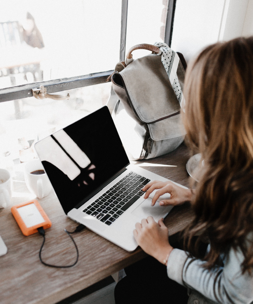 Woman in Denim Jacket Sitting at Coffee Shop Table with MacBook Pro and Cup of Coffee