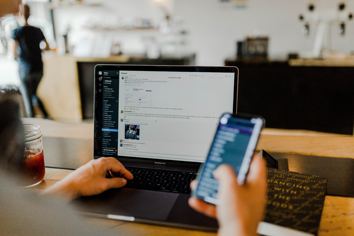 Man's Hand on MacBook Pro Keyboard with Screen Displaying Chat Interface, Other Hand Holding Smartphone