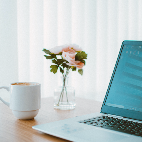 Laptop on Wooden Table with White Coffee Cup and Pink Flowers in Vase