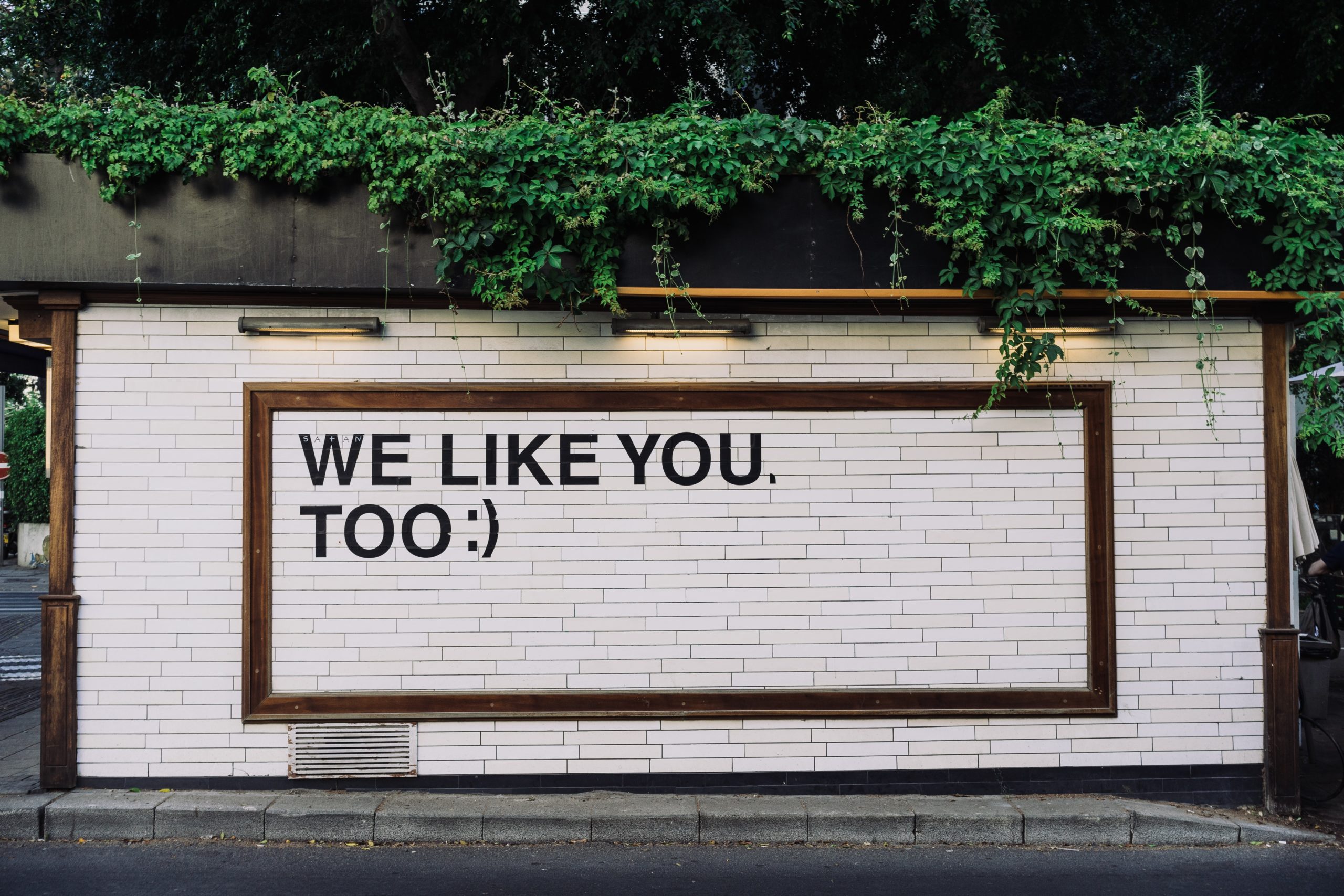 White Brick Building with "We Like You, Too" Decal Written in Black Letters