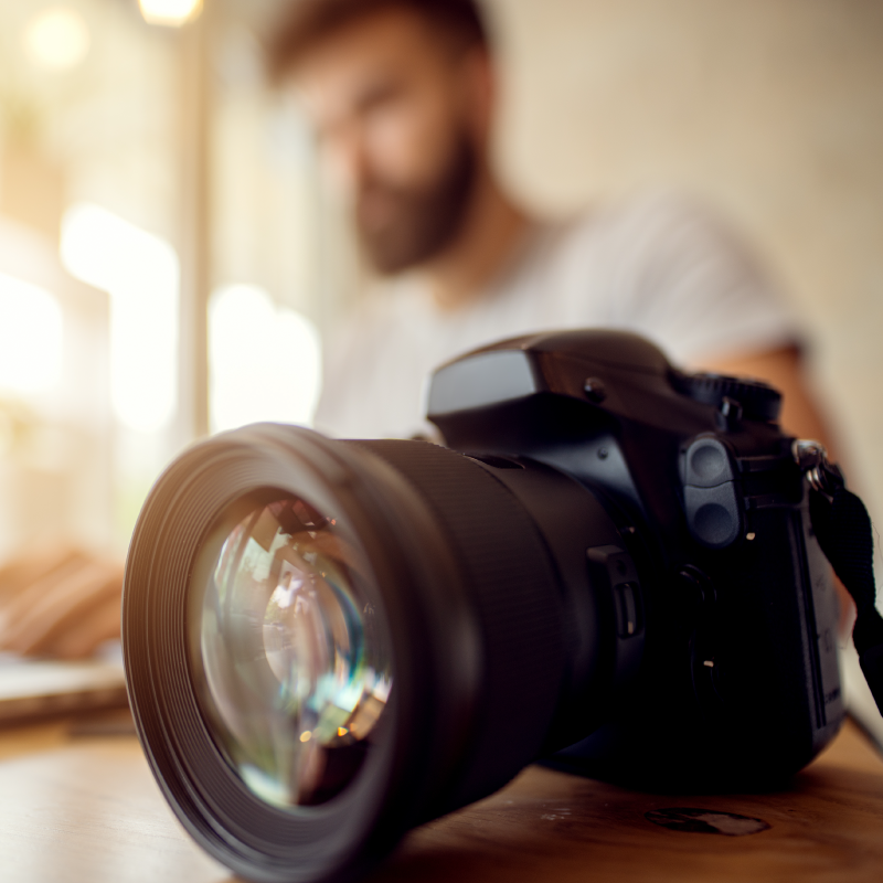 DSLR camera in foreground, blurred male photographer sitting at laptop in background