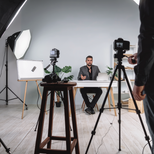 Photographer with camera on tripod in foreground, man posed at a desk for styled photo shoot in background