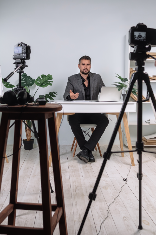 Photographer with camera on tripod in foreground, man posed at a desk for styled photo shoot in background