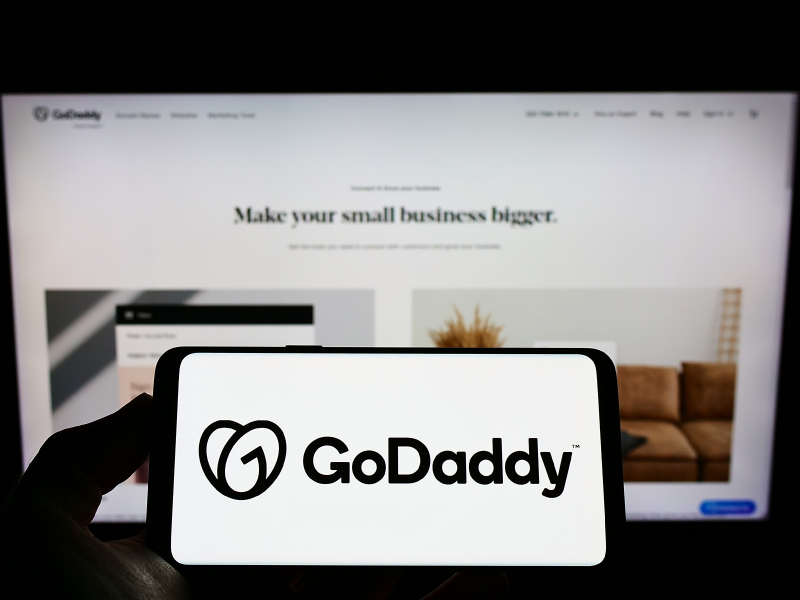 GoDaddy Logo on Smartphone Screen with Website on Desktop in Background