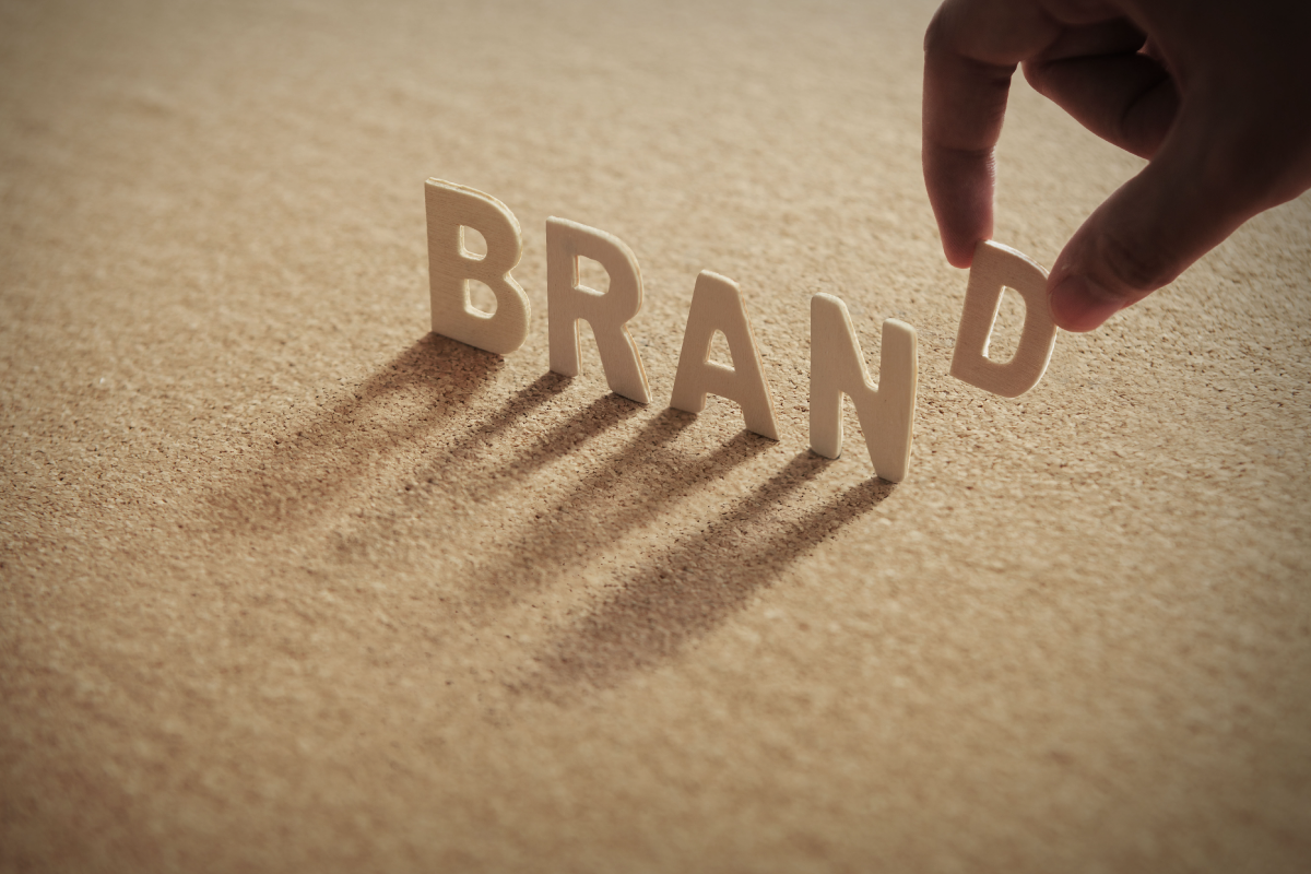 BRAND wooden word cutout on cork board with person's fingers holding D letter