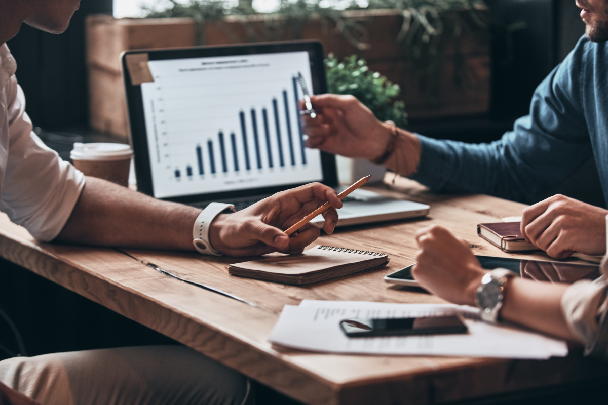 Three Office Workers Sitting at Desk with Marketing Graph on Laptop Screen